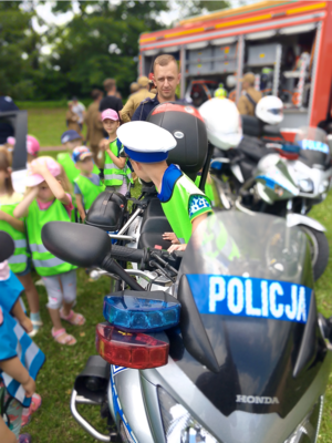 Przedszkolak w policyjnej czapce na policyjnym motocyklu. Na zdjęciu również pozostałe dzieci biorące udzial w profilaktyce