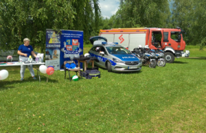 Wóz strażacki, policyjne motocykle oraz radiowóz, banery oraz stanowisko i pracownik sanepidu