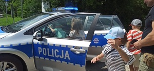 grupa dzieci oglądająca i wsiadająca do policyjnego radiowozu