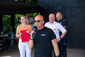 Komendant Powiatowey Policji w Wieliczce, przemawia ze sceny. Obok pozostali organizatorzy pikniku.