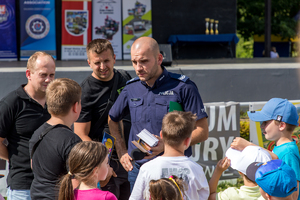 Policjant romzawia z uczestnikiem pikniku, obok stoji dwóch mężczyzn oraz dzieci