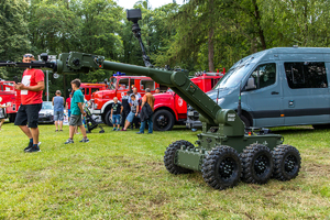 Policyjny robot, w tle wozy strażackie i uczestnicy pikniku.