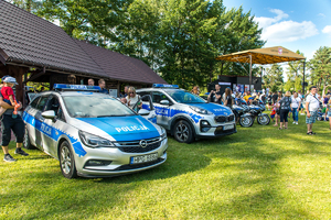 Radiowozy oraz motocykle policyjne, obok uczestnicy pikniku