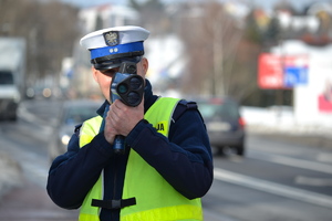 Policjant ruchu drogowego mierzący ręcznym miernikiem prędkośc pojazdów. Warunki zimowe