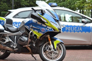 Motocykl policyjny z lietrą R za nim radiowóz policyjny