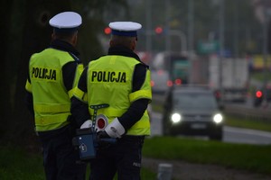 Dwóch policjantów ruchu drogowego stoi przy drodze, nadzoruje ruch.