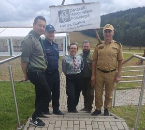 Pprzedstawiciele policji, straży pożarnej i harcerze stoją przy wejściu do obozowiska