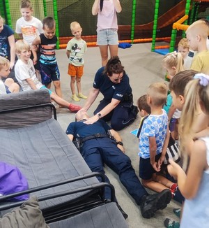 Policjanci podczas zajęć z dziećmi w parku rozrywki  policjantka pokazuje dzieciom sposób udzielania piwreszej pomocy