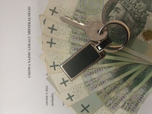 widać gotówkę oraz klucz położone na kartce z napisem umowa najmu lokalu mieszkalnego.