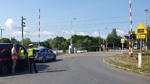 Na zdjęciu przejazd kolejowy, po lewej stronie oznakowany radiowóz i samochód Straży Ochrony Kolei obok którego stoi policjant ruchu drogowego, funkcjonariusz Straży Ochrony Kolei oraz przedstawiciel Polskicj Kolei