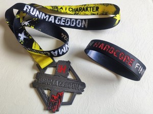 Po lewej stronie medal za udział w biegu Runmageddon obok opaska gumowa z napisem Runmageddon