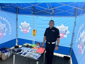 5 policjant przy stoisku profilaktycznym. Na stoliku tematyczne ulotki informacyjne