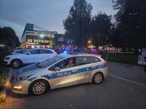 Policjanci w radiowozie przy deptaku prowadzącym na stadion którym idą kibice