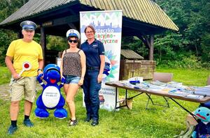 dwie osoby dorosłe pozują do zdjęcia w czapkach policyjnych z policjantką i maskotką policyjną