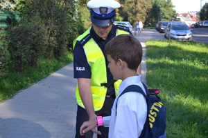 Policjant Ruchu Drogowego zapinający dziecku odblask na prawy nadgarstek...