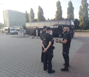 Na pierwszym tle policjanci zabezpieczający wyjazd kibiców, w tle autokar