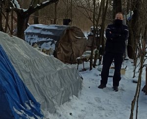 policjant w miejscu, gdzie przebywają bezdomni, obok namioty zamieszkiwane przez bezdomnych