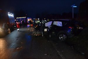 miejsce wypadku drogowego w Dąbrowie Szlacheckiej-pojazd leżący częściowo w rowie, w tle ratownicy i straż pożarna