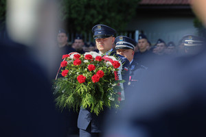 policjant niesie wiązankę kwiatów pod krzyż