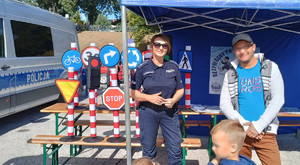 policjantka z mężczyznom stoją przy policyjnym stoisku, w tle radiowóz i znaki drogowe z mini miasteczka rowerowego