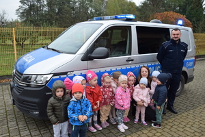 Policjant wpólnie z przedszkolakami na tle radiowozu