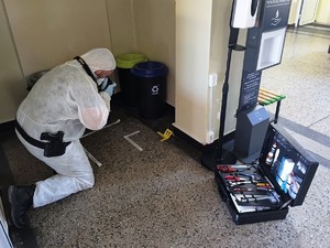 Policjant ubrany w biały kombinzon wykonujący oględziny na miesjcu zdarzenia.