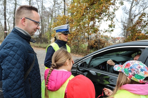 dzieci z opiekunem i policjantką podczas rozmowy z kierowcą samochodu