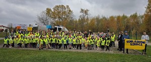 Grupa dzieci w kamizelkach odblaskowych oraz nauczyciele a także umundurowani policjanci. W tle radiowóz.