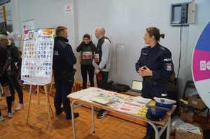 dwóch umondurowanych policjantów z dwojką uczestników zawodów stąjący przy stoisku profilaktyczno edukacyjnym