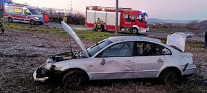 Miejsce zdarzenia śmiertelnego wypadku drogowego. Widać samochód volkswagen koloru szarego, w tle wóz strażacki ora karetke pogotowia.