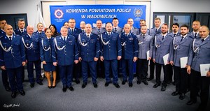 Na zdjęciu grupa umundurowanych policjantów i policjantek stojacych na tle policyjnego baneru z napisem Komenda Powiatowa policji w Wadowicach.