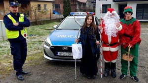 Na zdjęciu umundurowany policjant, a obok radiowozu stoją dzieci pzrebrane za Mikołaja, elfa i diabła.