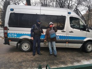 Funkcjonariusz policji przekazuje buty mężczyźnie. W tle radiowóz Oddziału Prewencji Policji w Krakowie