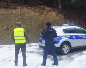 funkcjonariusz i strażnik leśny rozpoczynają kontrolę, obok oznakowany radiowóz