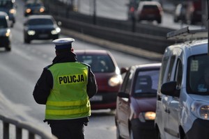 Policjant stoi na poboczu drogi i obserwuje jadące samochody
