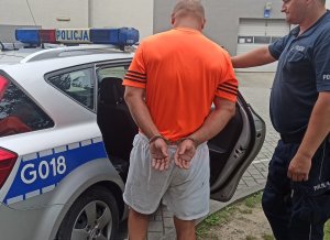 zatrzymany mężczyzna doprowadzany przez policjanta do radiowozu