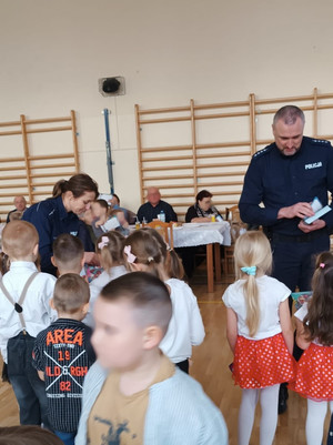 dwoje policjantów rozdających ulotki dzieciom na sali gimnastycznej w szkole