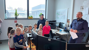 dzieci przy stanowisku dowodzenia na dużyrce komendy przed nimi dyyżurny obok policjantka