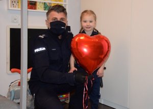 Komendant Miejski Policji pozuje z dziewczynką do wspólnego zdjęcia, trzymając balon w kształcie czerwonego serca