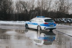Fotografia przedstawia perspektywę radiowozów policyjnych. Widoczne są warunki zimowe – nawierzchnia mokra pokryta częściowo śniegiem i lodem.