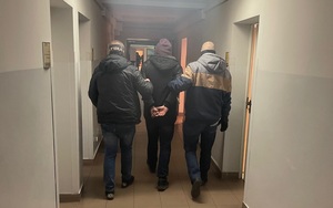 nieumundurowani policjaci prowadzą zakutego w kajdanki zatrzymanego mężczyznę korytarzem w komisariacie policji