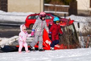 Trójka dzieci trzymająca sie za ręce ubrane w stróje narciarskie