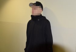 zatrzymany mężczyzna ubrany w czarną bluzę oraz czapkę z daszkiem stojący przodem do zdjęcia