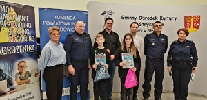 Na zdjęciu policjantka i dwóch policjantów oraz kobieta i dwóch mężczyzn w stroju cywilnym, a także dziewczyna i chłopak, którzy trzymają w ręku dyplomy i upominki. W tle banery.