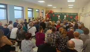 Na zdjęciu grupa osób siedzących na krzesłach  Osoby są tyłem  Przed nimi jest umundurowany policjant