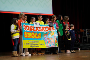 kolorowo ubrane dzieci z nauczycielką trzymający w rękach duży kolorowy baner z napisem odblaskowa szkoła