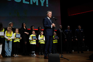 Małopolski Wicekurator Oświaty przemawia na scenie, w tle stojące dzieci