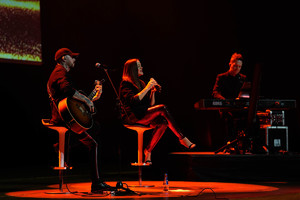 Spiewająca kobita siedzi na krześle w tle grający na instrumentach muzycy