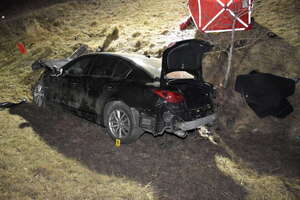 Rozbity samochód stoi w przydrożnym rowie na trawie z otwartym bagażnikiem