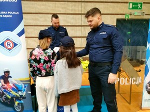 policjant wręczają dzieciom ulotki przy stoisku profilaktycznym sądeckiej komendy